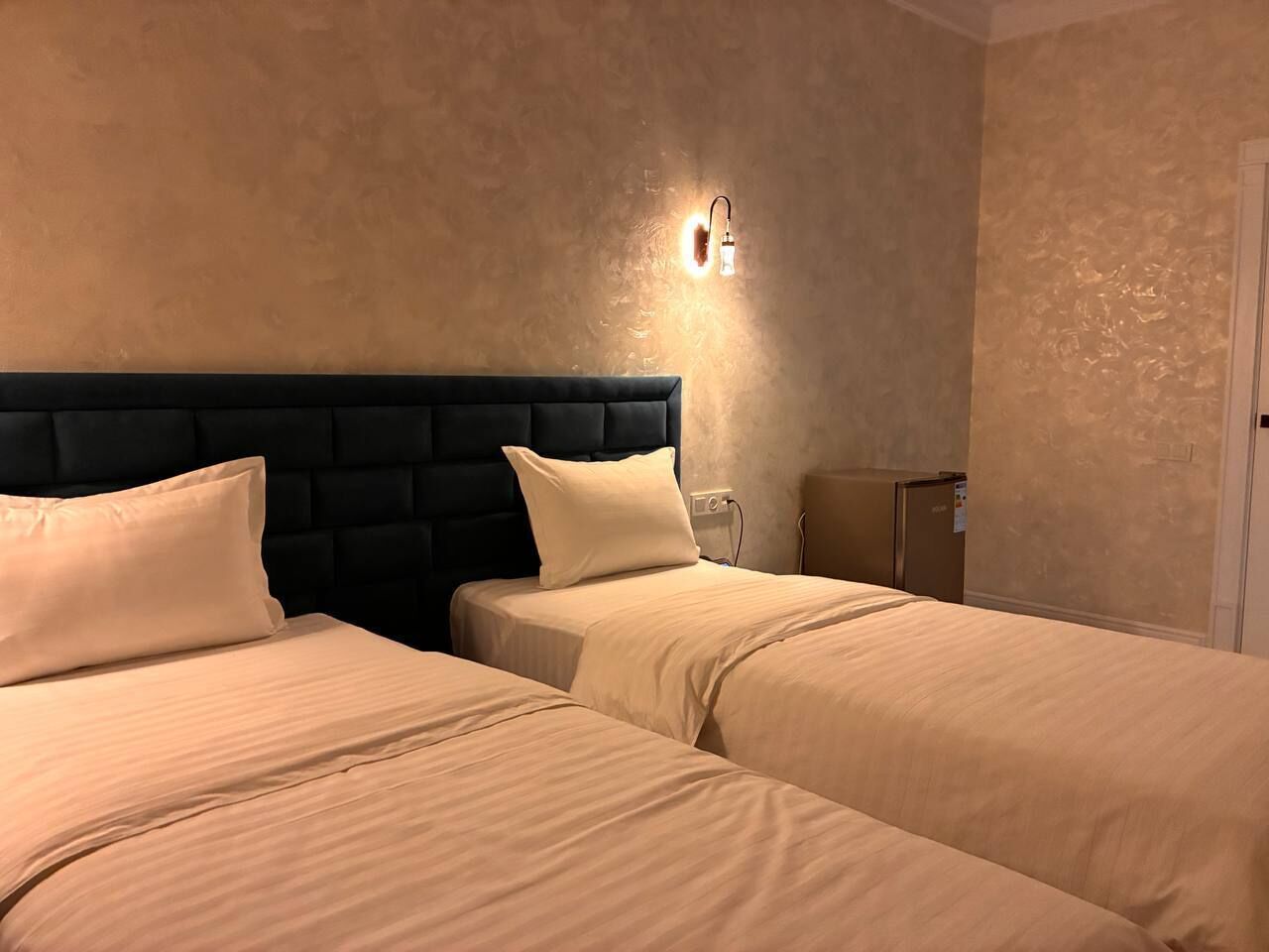 A hotel room with two beds, a dark headboard, and a wall-mounted light fixture.