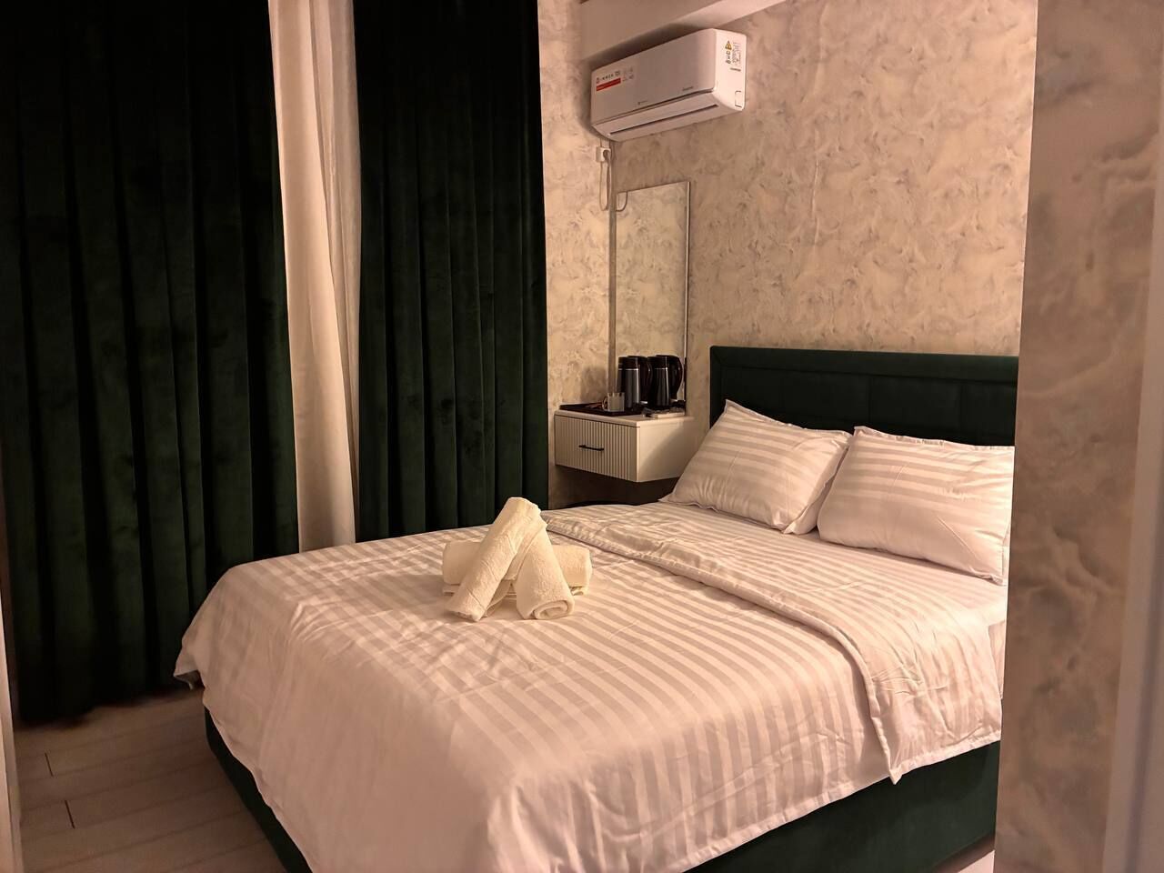 A hotel room with a bed, a nightstand, a mirror, and an air conditioning unit.