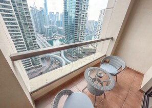 A balcony with a glass railing, two wicker chairs, and a small table. - StayShort - Chic Apartment in JBR Sleeps 3 with Canal View! (Jumeirah Beach Residence)