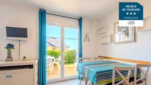 A room with a dining table, chairs, a TV, and a view of the outside. - Peaceful Coastal Stay With Access to Pool (Saint-Nic)
