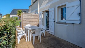 A patio with a table and chairs, a wooden fence, and a house with a window and a door. - Peaceful Coastal Stay With Access to Pool (Saint-Nic)