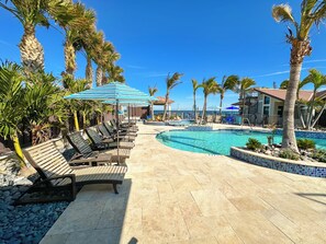 A poolside area with lounge chairs and umbrellas, a clear blue sky, and a view of the ocean. - The Rod and Reel Resort-Suite 7 (Anna Maria)