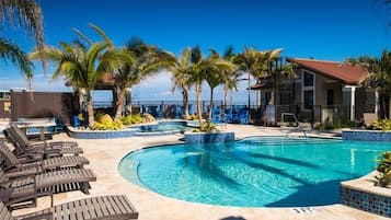 A swimming pool with lounge chairs, palm trees, and a building with a red roof.