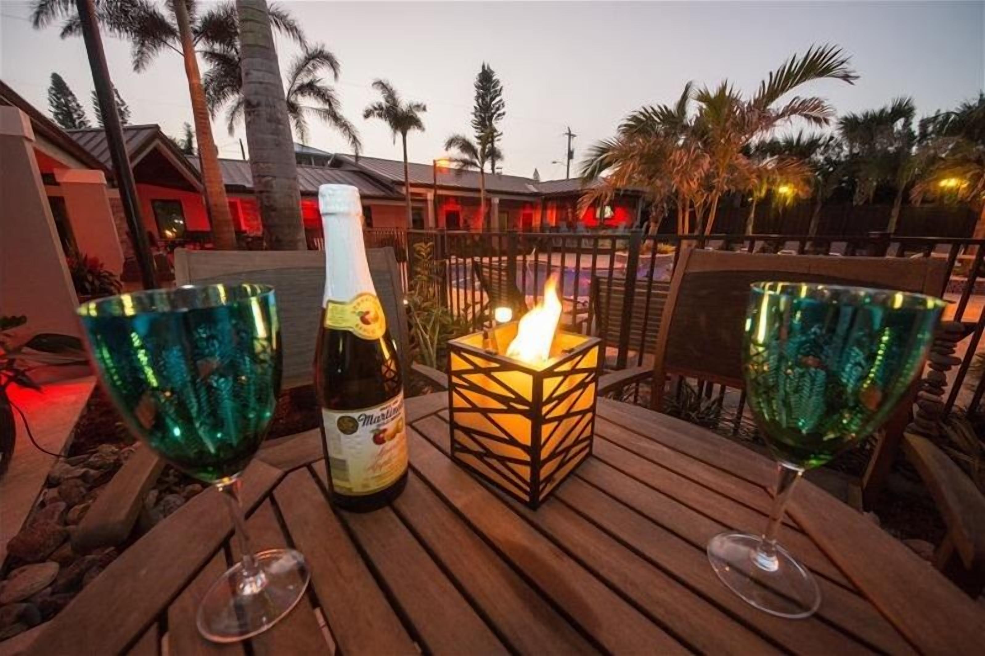 A wooden table with two green glass wine glasses, a bottle of Martini, and a lit candle in a square lantern.