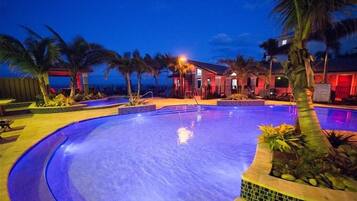 A swimming pool with a curved edge, surrounded by palm trees and a building with red lighting.
