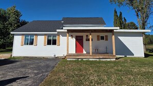 A single-story house with a red door, a covered porch, and a small table. - Beautiful, newly renovated 4-bedroom, 2 bath farmhouse in the Petoskey area (Petoskey)