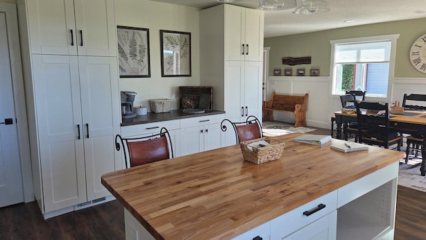 A kitchen with white cabinets, a wooden island, pendant lights, and a dining area with a bench and chairs. - Beautiful, newly renovated 4-bedroom, 2 bath farmhouse in the Petoskey area (Petoskey)