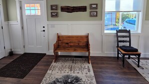 A room with a wooden bench, a chair, a door with a window, and a wall-mounted picture frame. - Beautiful, newly renovated 4-bedroom, 2 bath farmhouse in the Petoskey area (Petoskey)