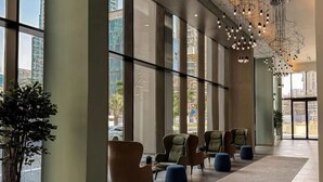Un'ampia hall con grandi vetrate, poltrone moderne e un lampadario geometrico al soffitto.