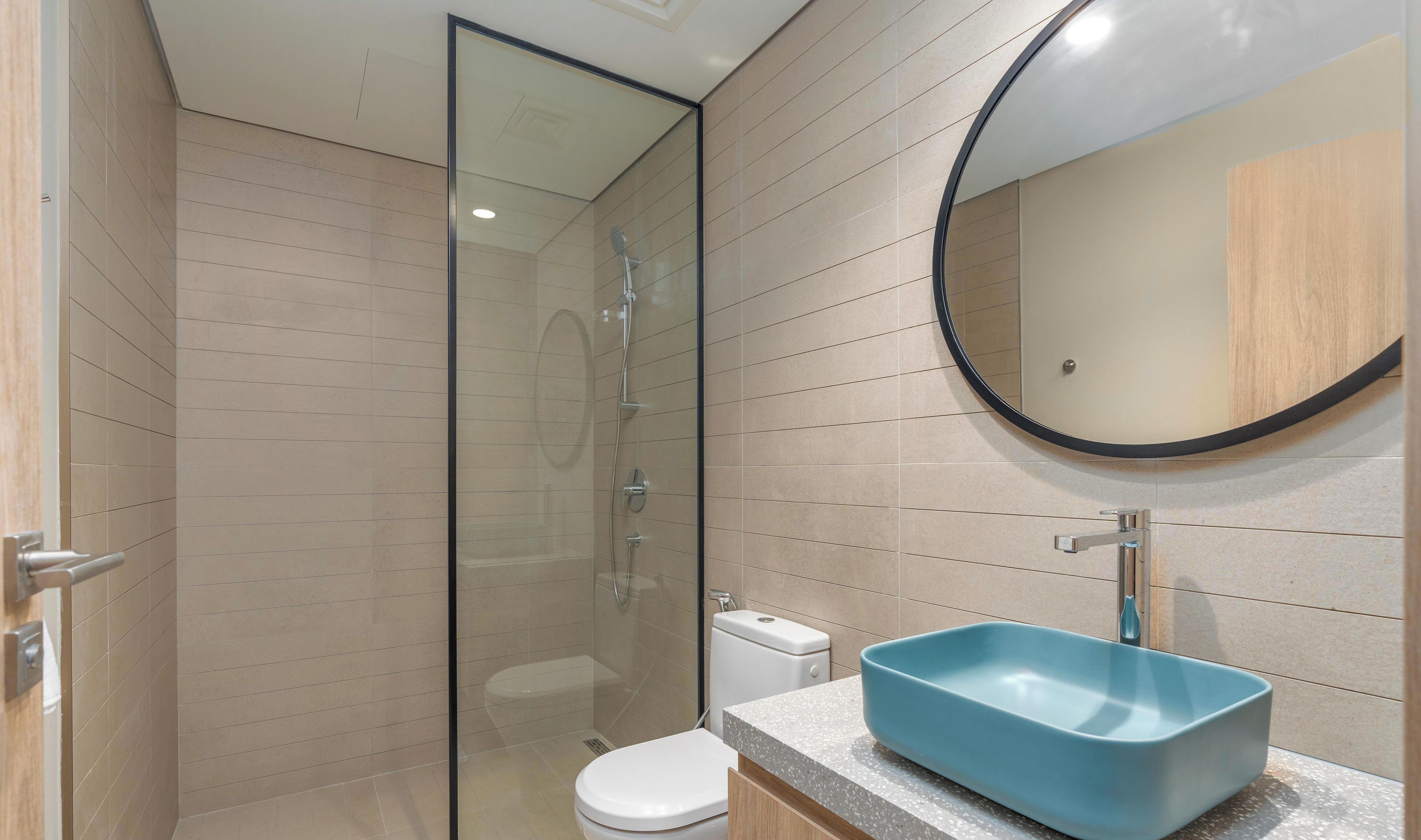 A modern bathroom with a glass-enclosed shower, a white toilet, and a blue sink on a speckled countertop.