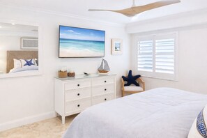 A bedroom with a bed, a dresser, a chair, a ceiling fan, a window with blinds, and a beach-themed painting on the wall. - Beachfront, Dolphins,North End, walk to Margaritaville, Shelling (Fort Myers Beach)