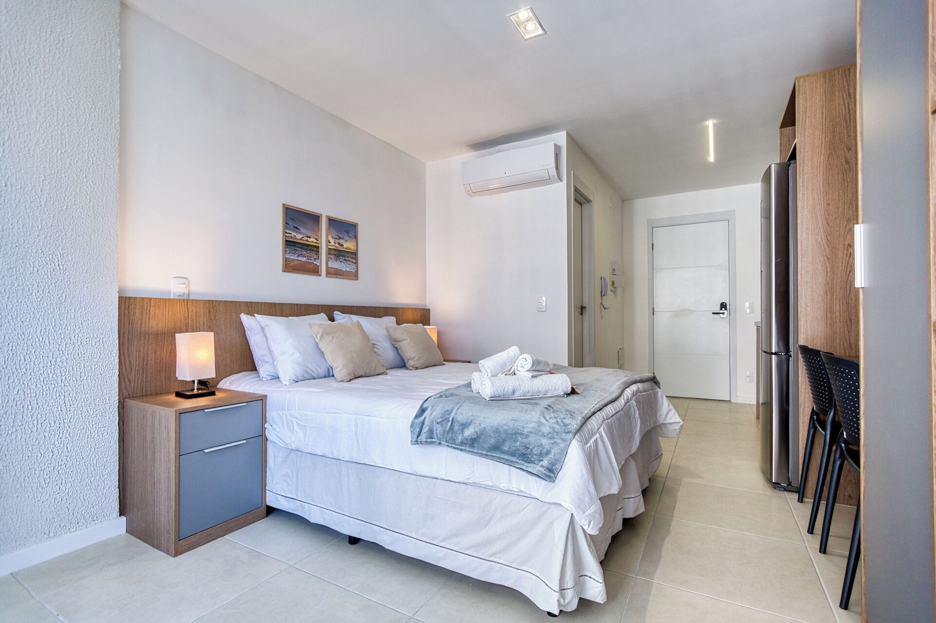 Une chambre d’hôtel équipée d’un lit, d’une table de chevet, d’une lampe, d’un climatiseur et d’une porte donnant accès à une salle de bain.