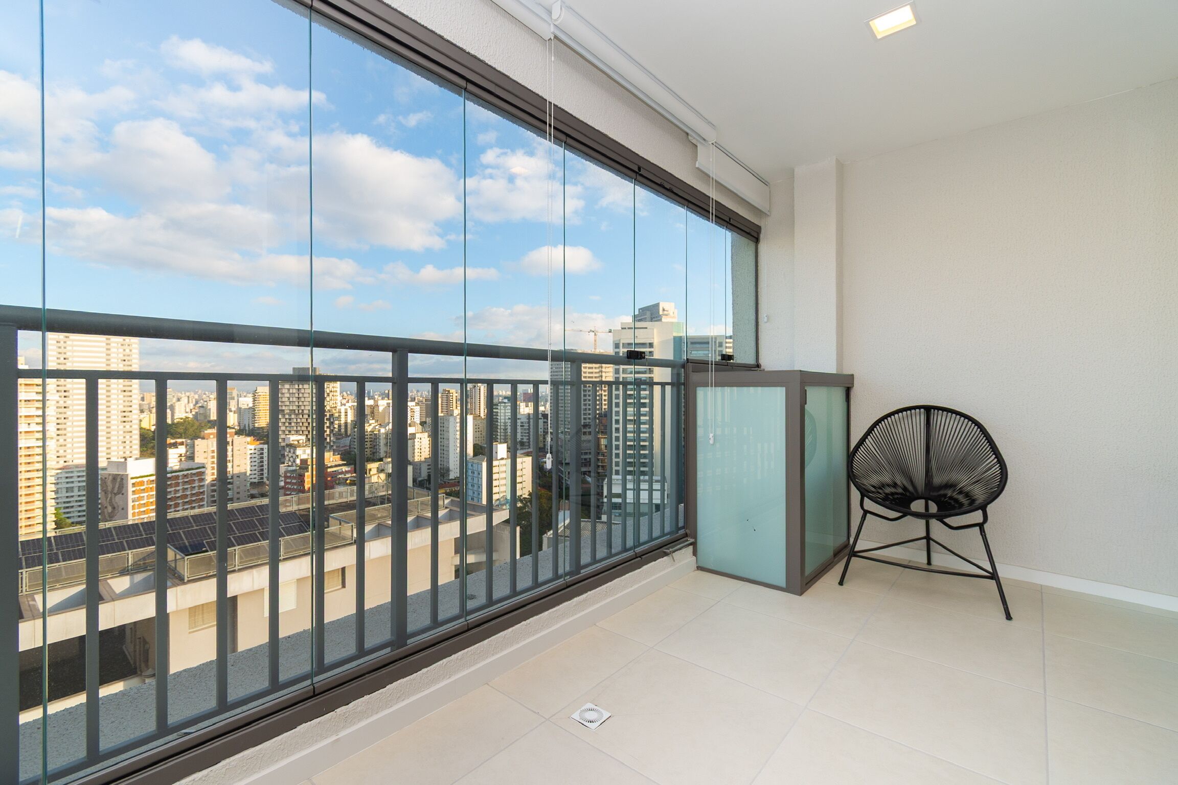 A balcony with a view of a cityscape, a chair, and a small table.