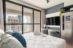 A modern hotel room with a large bed, a seating area, a TV, and a balcony with a city view. - 360 The Collection Madalena (São Paulo)