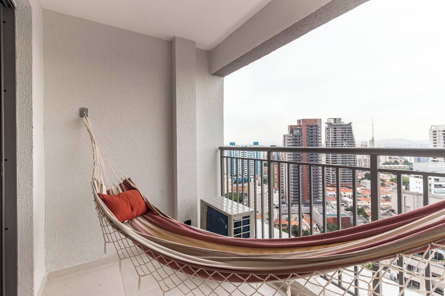 Un balcon avec un fauteuil suspendu, une rambarde en métal et une vue sur la ville.