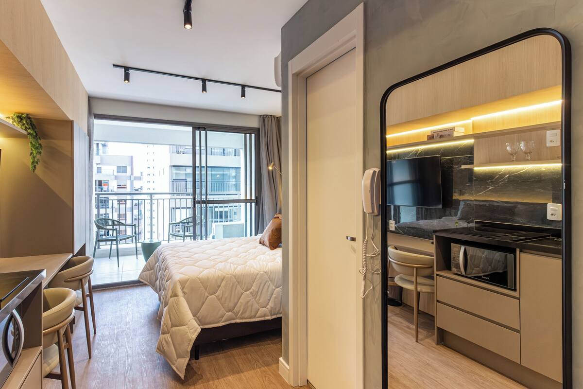 Une chambre d’hôtel moderne équipée d’un lit, d’un bureau et d’une kitchenette. Elle dispose également d’un balcon avec vue sur la ville.