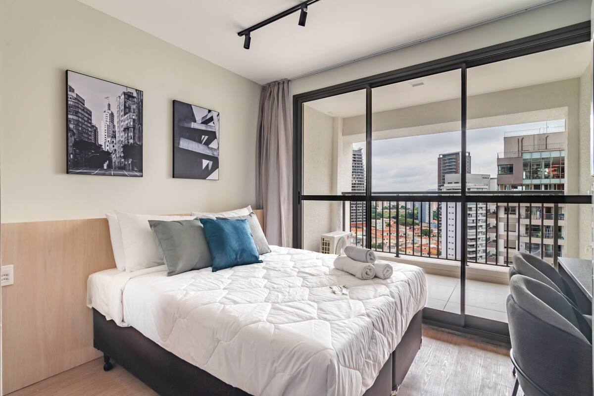 Une chambre d’hôtel avec un grand lit, un balcon donnant sur la ville et deux tableaux encadrés au mur.