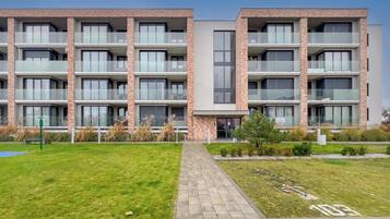 Un immeuble résidentiel à plusieurs étages, doté de balcons, d’une allée pavée et d’un petit espace jardin.