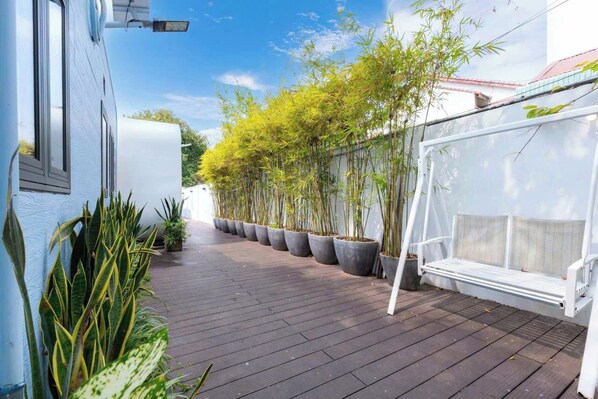Una terraza de madera con plantas de bambú en macetas y un banco blanco.