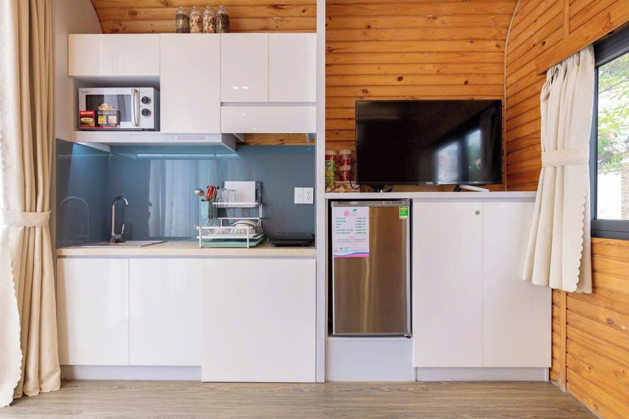 A compact kitchen with white cabinets, a microwave, a refrigerator, and a flat-screen TV.