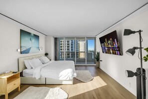 Un dormitorio moderno con una cama grande, un escritorio, un cuadro de un paisaje urbano y un ventanal con vistas a rascacielos.