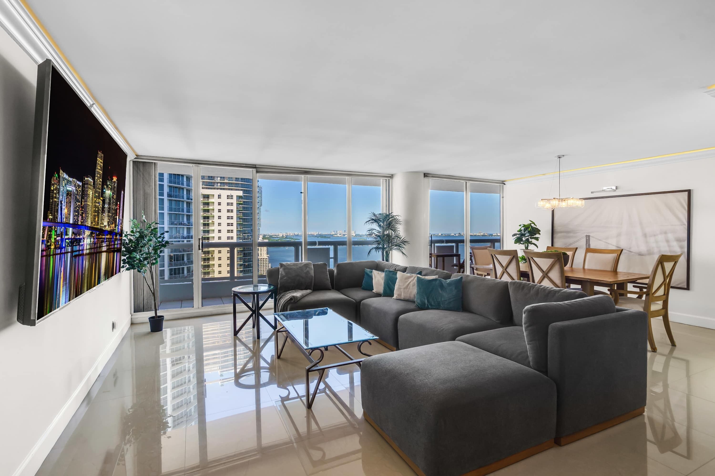 A modern living room with a sectional sofa, a glass coffee table, and a dining area with a wooden table and chairs.