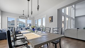 A spacious dining area with a long wooden table, multiple chairs, and pendant lighting. - 33555 Misty Moon Drive - Large Home in The Peninsula (Millsboro)