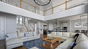 A spacious living area with a high ceiling, a staircase, and a kitchen in the background. - 33555 Misty Moon Drive - Large Home in The Peninsula (Millsboro)