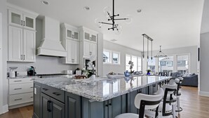 A modern kitchen with a large island, white cabinetry, and a bar area with stools. - 33555 Misty Moon Drive - Large Home in The Peninsula (Millsboro)