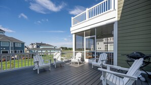 A covered deck with white Adirondack chairs and a grill, overlooking a green lawn and neighboring houses. - 33555 Misty Moon Drive - Large Home in The Peninsula (Millsboro)