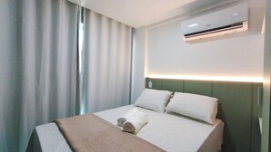 Une chambre d’hôtel avec un lit, une fenêtre avec des rideaux, un appareil de climatisation et un luminaire fixé au mur.