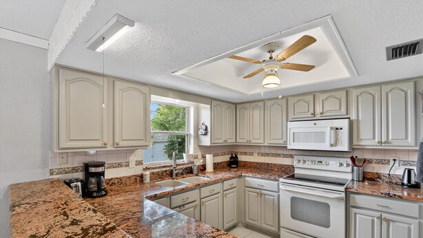 A kitchen with white cabinets, granite countertops, a built-in oven, and a ceiling fan. - Chelsea Way Getaway Bright 4br Family Retreat 4 Bedroom Home (Port Orange)