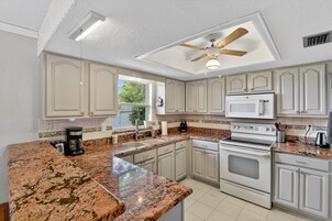 Una cocina con armarios blancos, encimeras de granito, horno empotrado y ventilador de techo.