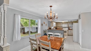 A dining area with a wooden table and chairs, a chandelier, and a view of the kitchen in the background. - Chelsea Way Getaway Bright 4br Family Retreat 4 Bedroom Home (Port Orange)