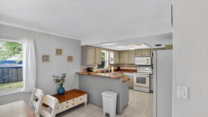 A kitchen with a central island, white cabinets, and a dining area with a wooden table and chairs. - Chelsea Way Getaway Bright 4br Family Retreat 4 Bedroom Home (Port Orange)