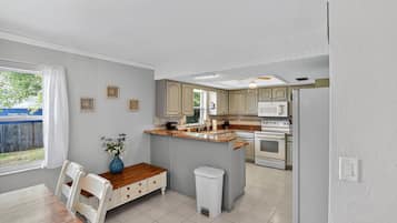 A kitchen with a central island, white cabinets, and a dining area with a wooden table and chairs.