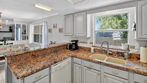 A kitchen with granite countertops, white cabinetry, a coffee maker, and a window with a view of trees. - Chelsea Way Getaway Bright 4br Family Retreat 4 Bedroom Home (Port Orange)
