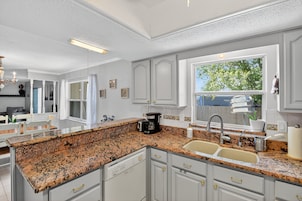 A kitchen with granite countertops, white cabinetry, a coffee maker, and a window with a view of trees.