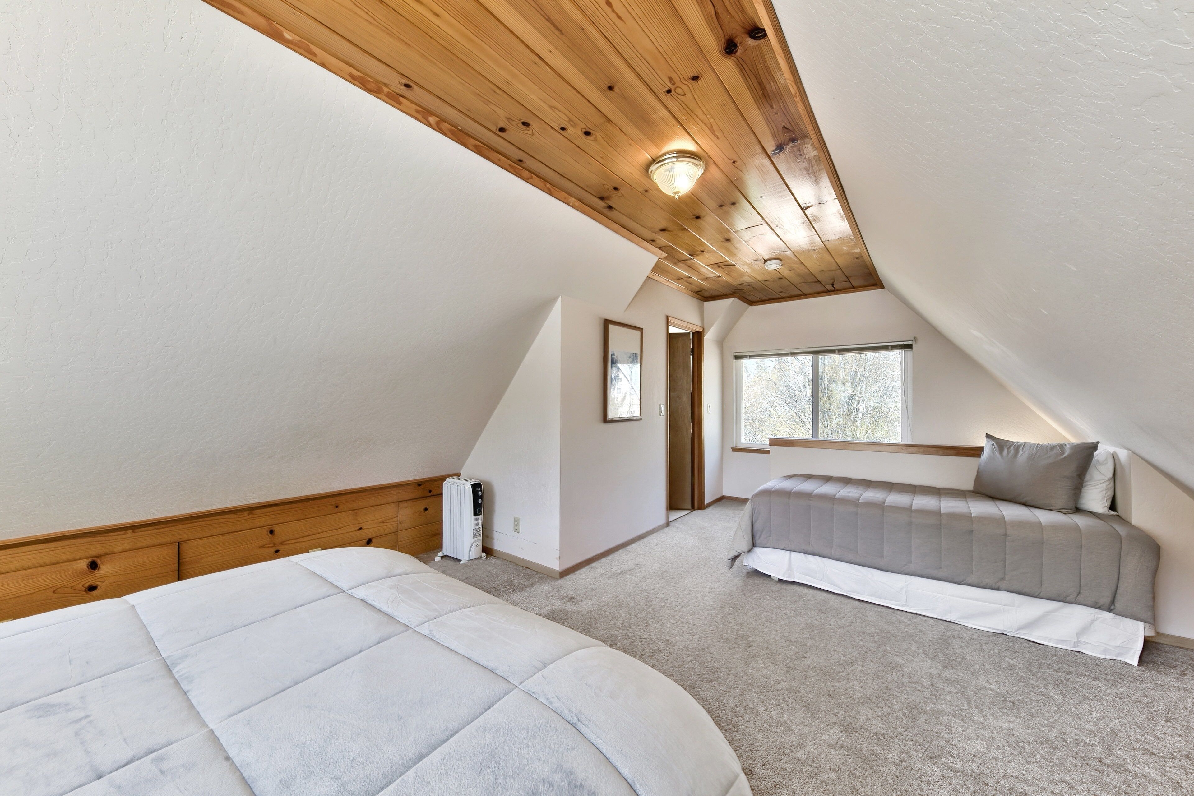 Une chambre avec un plafond en pente, un lit, une table de chevet, un radiateur et une fenêtre.