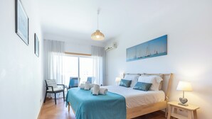 Et hotelværelse med seng, stol, skrivebord, lampe og et maleri på væggen.
