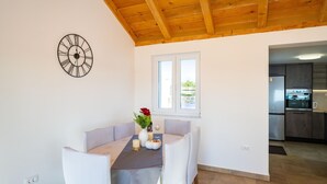 A dining area with a table set for two, a clock on the wall, and a window with a view of the outside. - Holiday Home in Rtina for 4 Guests (Razanac)