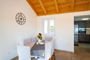 A dining area with a table set for two, a clock on the wall, and a window with a view of the outside. - Holiday Home in Rtina for 4 Guests (Razanac)