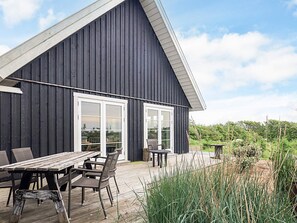 A dark wooden building with a sloped roof, large windows, and a wooden deck with outdoor furniture. - 4 Star Holiday Home in Ranum (Ranum)
