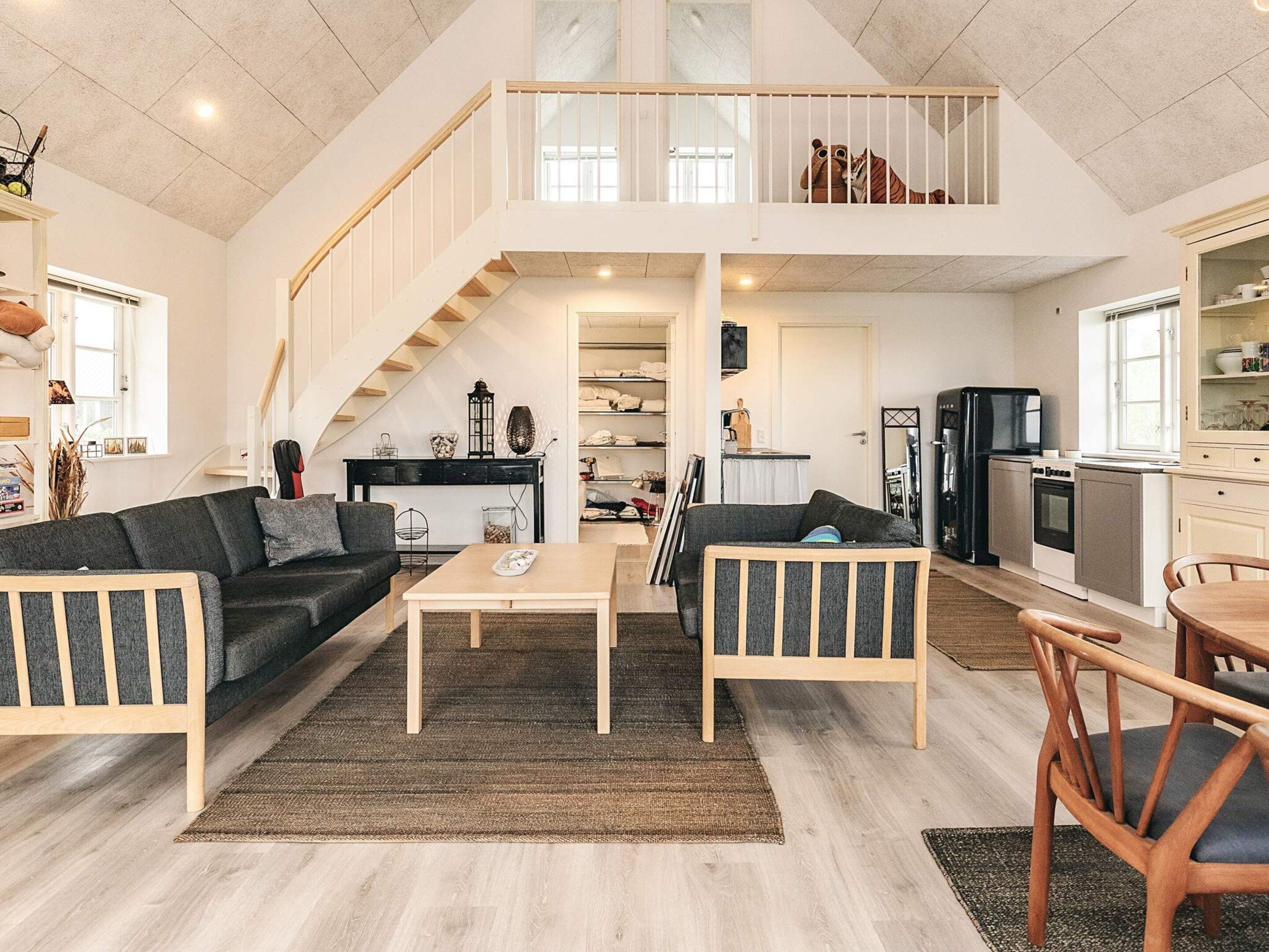 Egy tágas nappali magas mennyezettel, egy felső szintre vezető lépcsőházzal, valamint modern berendezésekkel felszerelt konyha.