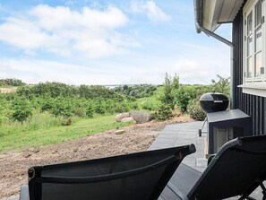 Un patio con mobiliario exterior, una parrilla y vistas a un paisaje verde.