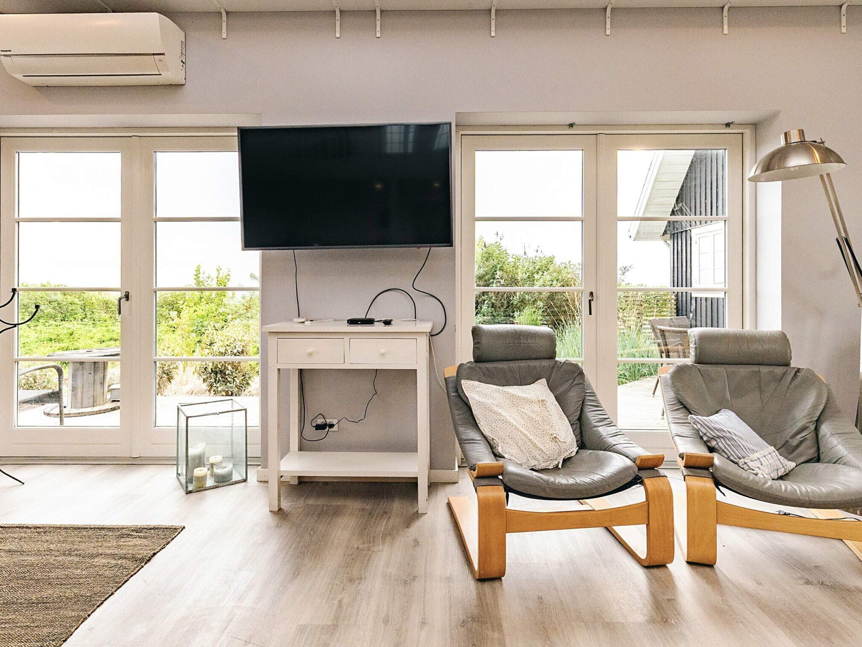 A living room with a flat-screen TV, two leather armchairs, a small white console table, and a floor lamp.