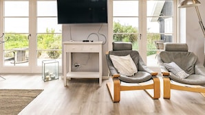 Un salon équipé d’un téléviseur à écran plat, de deux fauteuils en cuir, d  ’une petite console blanche et d’un lampadaire.