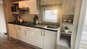 A compact kitchen with white cabinets, a black countertop, a built-in stove, and a window with blinds. - RBR 433 - Beach Resort Kamperland (Kamperland)