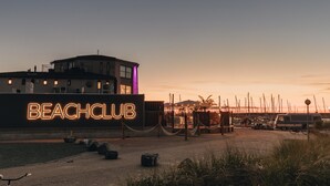A beach club with a neon sign, a building with multiple windows, and a dock area with boats. - RBR 433 - Beach Resort Kamperland (Kamperland)