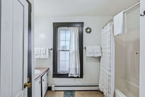 Ein Badezimmer mit Fenster, Handtuchhalter, Duschvorhang und Heizkörper.
